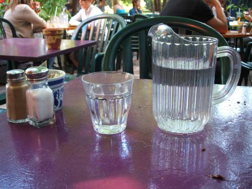 Plastikkanne und Glas mit Leitungswasser auf dem Tisch eines Gartenlokals. Foto: Paul Morf Gronert